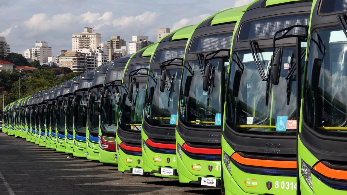 Frota de ônibus elétricos municipais alinhada em garagem com infraestrutura de eletropostos e recarga