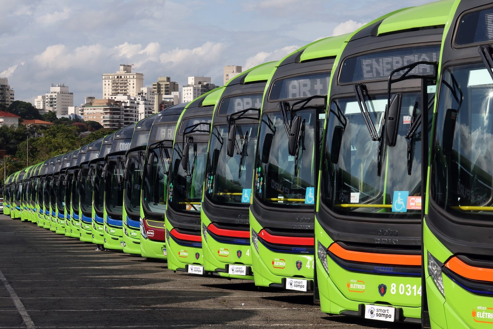 Frota de ônibus elétricos municipais alinhada em garagem com infraestrutura de eletropostos e recarga