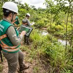 Fiscal e auditora ambiental de prefeitura analisando mapa georreferenciado e licença ambiental em tablet no campo