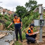 Agentes da Defesa Civil Municipal inspecionando sensor IoT de monitoramento em área de risco